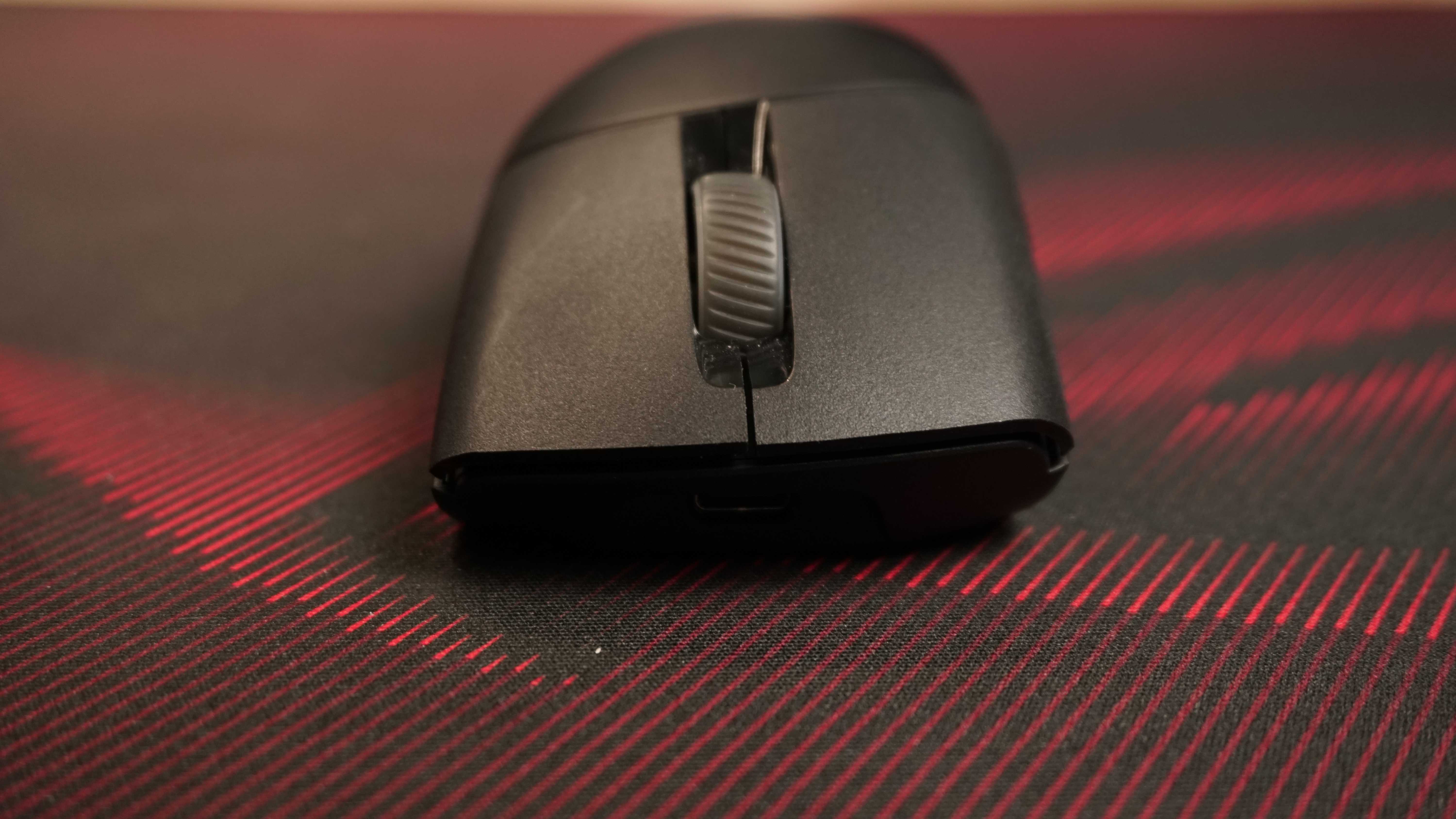 Front close-up of a black computer mouse showing its scroll wheel, on a dark textured surface with red light streaks