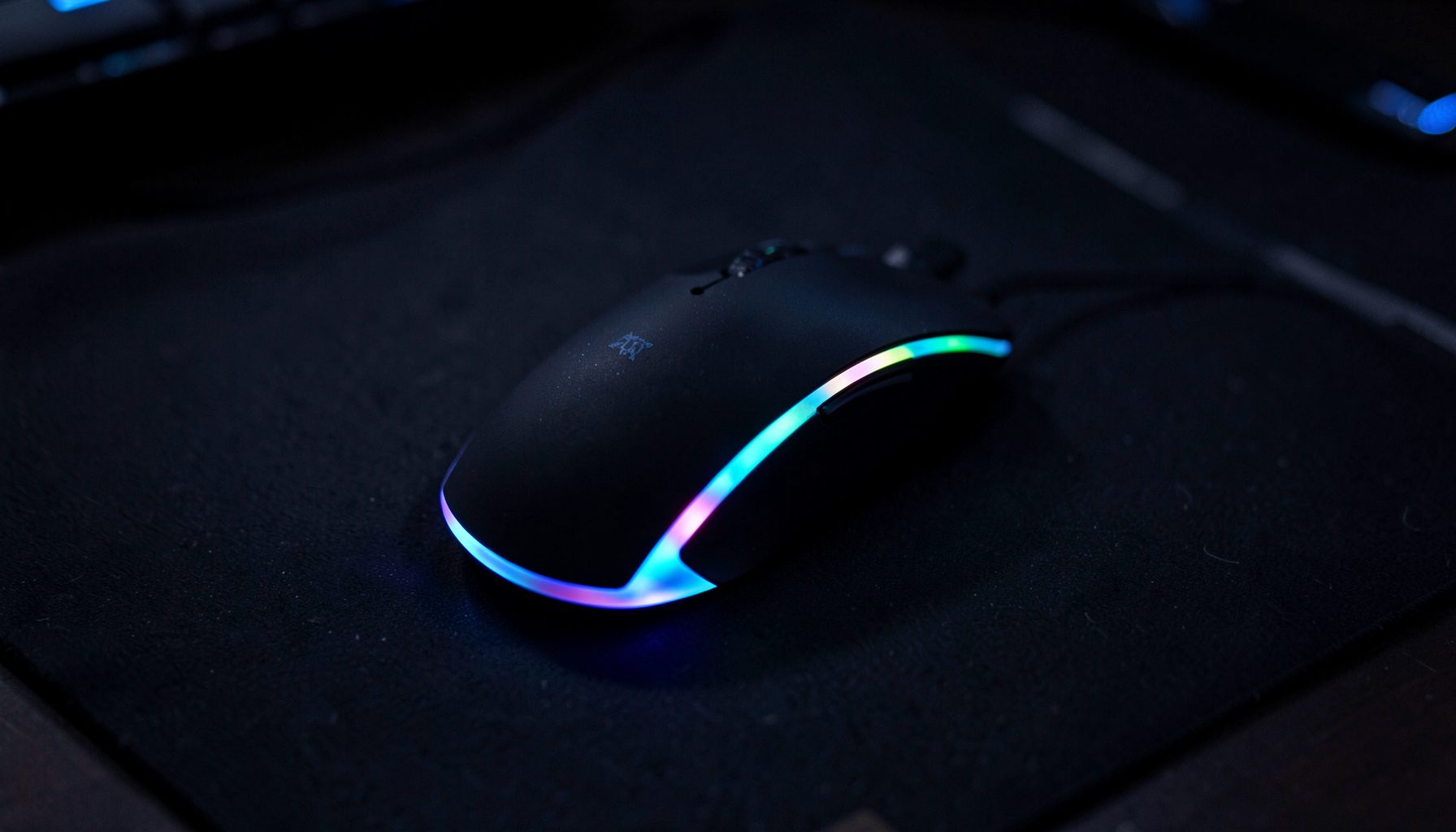 Gaming mouse with RGB accent lighting resting on a dark mousepad, dramatic side lighting