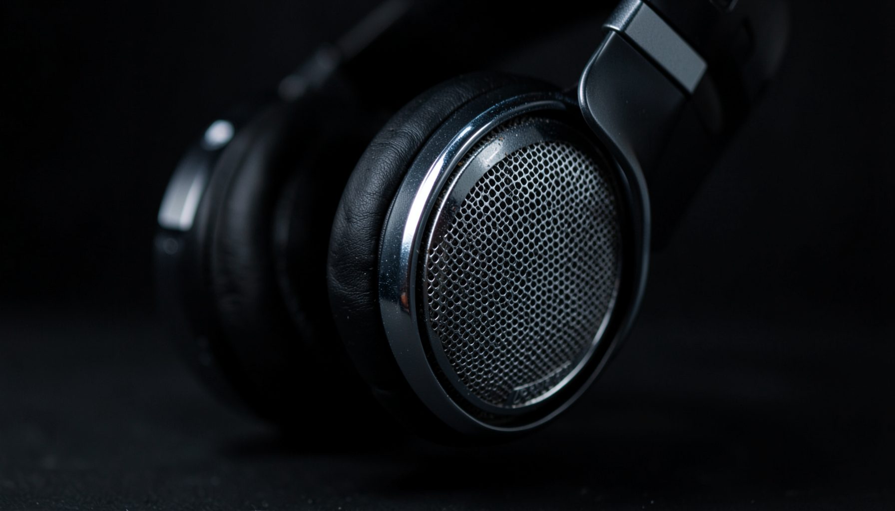 Dark atmospheric close-up of over-ear headphones with metallic grilles, moody studio lighting